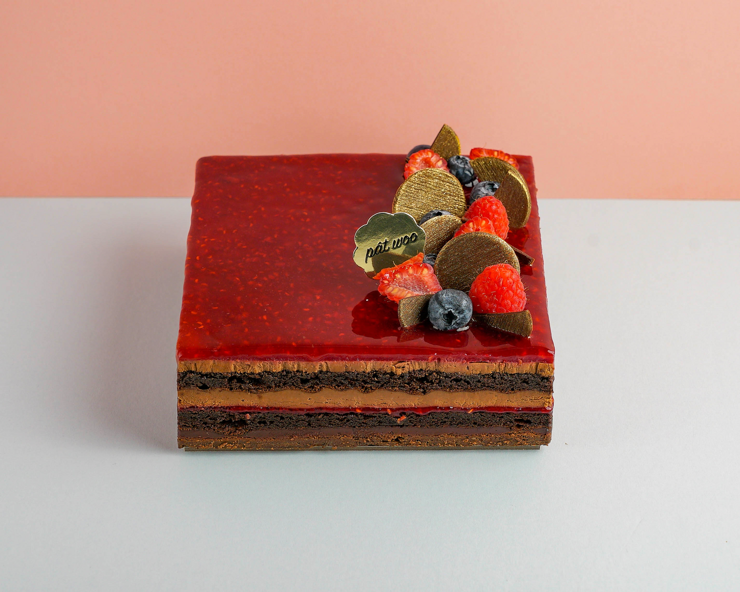 Layered chocolate cake decorated with fresh raspberries, blueberries and chocolate pieces, topped with a raspberry glaze.